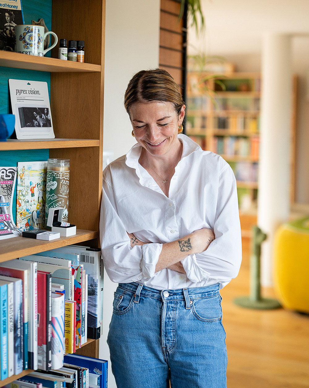 Eliza Fricker is Photographed mid-laugh standing by a bookcase in her home