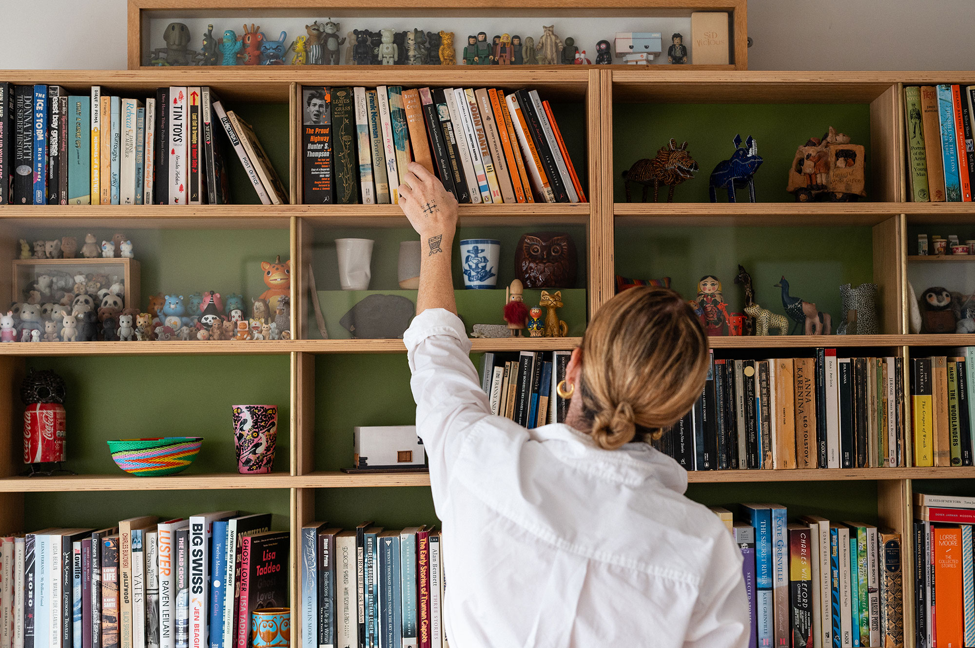 Eliza Fricker with her back to the camera selects a book from her bookshelf